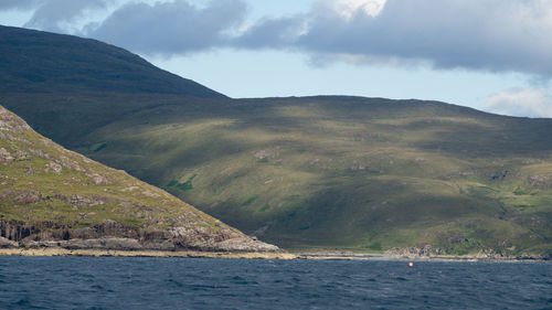 Scenic view of sea by mountain against sky