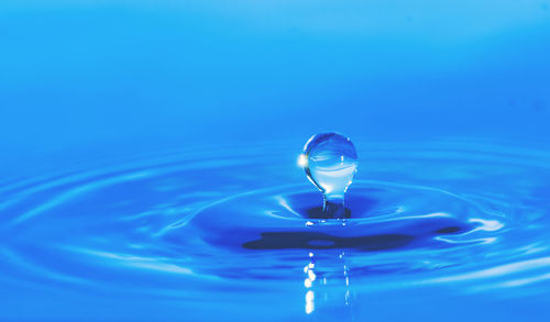 Close-up of drop falling on water against blue background