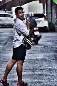 Side view portrait of man holding umbrella while standing on road during rainy season