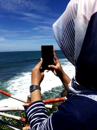 Low section of person photographing on sea against sky