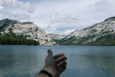 Cropped hand of man against lake by mountains