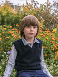 Caucasian boy with long hair is sitting outdoor near flowers and looking at camera. school uniform