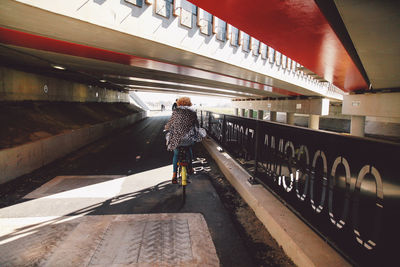 Rear view of woman riding bicycle on street under bridge