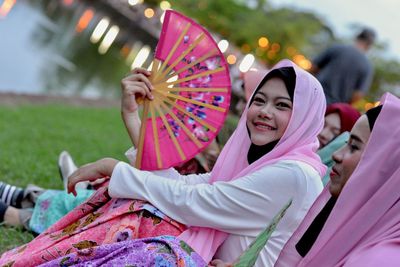 Woman with friends holding hand fan at park
