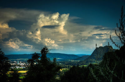 Trees on landscape against cloudy sky