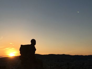 Silhouette man standing on rock against sky during sunset