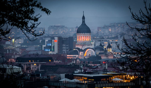 Illuminated buildings in city at dusk - avram iancu plaza in cluj napoca