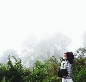 Young woman standing against trees amidst fog