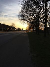 Road by trees against sky during sunset