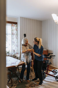 Female healthcare worker assisting senior woman while standing up at home