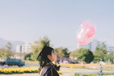 Side view of young woman holding balloon against sky