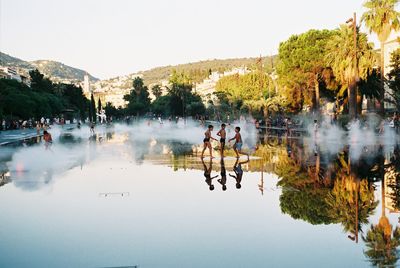 People by lake against clear sky