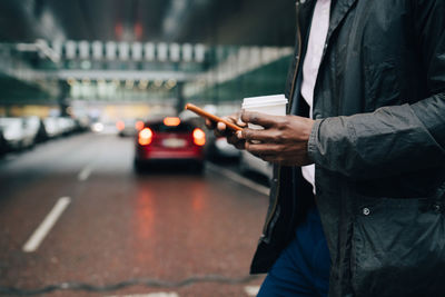 Man holding mobile phone while standing on street in city