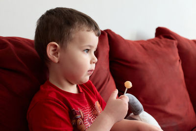 Cute little boy sitting on the couch holding a sugar candy
