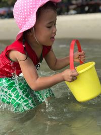 Girl playing with bucket while sitting at beach