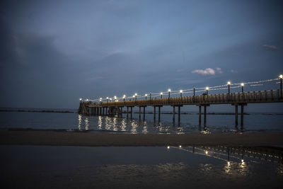 Illuminated bridge over sea against sky at night