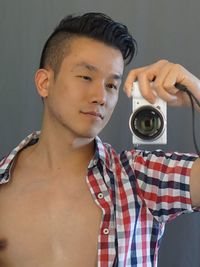 Man taking selfie with camera while standing against wall