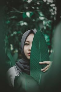 Portrait of young woman holding leaf over eye