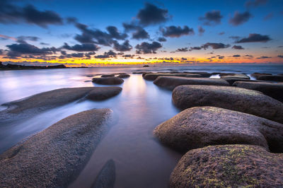 Stones at seashore against cloudy sky during sunset