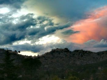 Low angle view of trees on mountain against dramatic sky