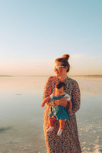 Happy smiling woman with red hair holding her child and walking by the sea