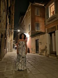 Portrait of woman standing against illuminated building at night