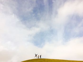 Three people on mountain against cloudy sky