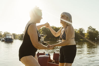 Rear view of woman with arms raised against lake