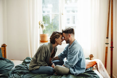 Couple touching foreheads while sitting on bed at home