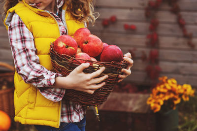 Midsection of girl holding wicker basket with apples