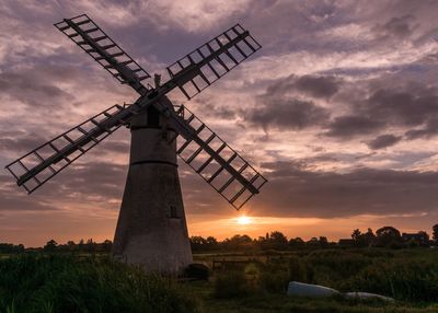 Traditional windmill on field against sky during sunset