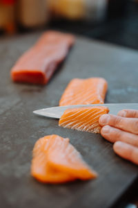 Vertical view of the hands of unknown man chief holding knife and cuts the salmon on wooden board