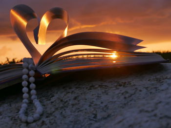 Bead necklace with heart shape folded pages of book during sunset