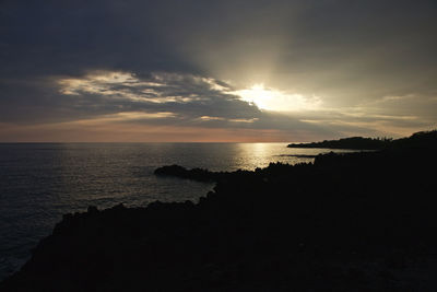 Silhouette landscape by sea against sky during sunset