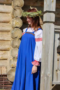 Young woman looking away standing against wooden wall