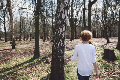 Rear view of young woman standing by tree on field