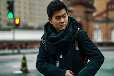 Young man looking away while standing on street in city during winter