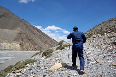 A tourist with trekking sticks climbs uphill, passing along river. upper mustang. nepal.