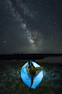 Woman relaxing on illuminated inflatable chair on field against star field