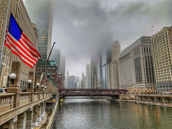 Bridge over river amidst buildings in city against sky