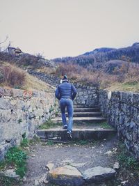 Rear view of man walking on mountain against clear sky