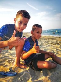 Portrait of brothers showing thumbs up signs at beach