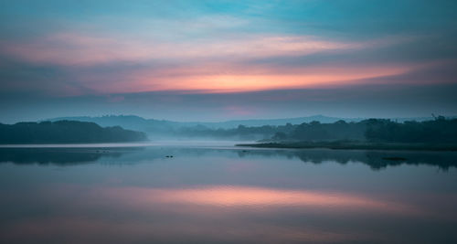 Scenic view of lake against dramatic sky during sunset