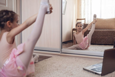 Pretty young ballerina practicing classic choreography during online class, social distance