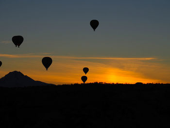 Silhouette hot air balloons flying in sky during sunset