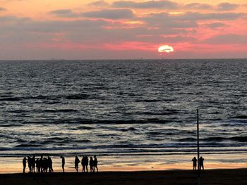 Silhouette people on beach against sky during sunset