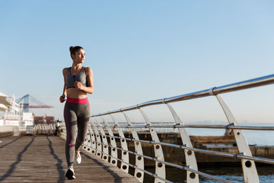 Full length of woman jogging by railing against clear sky