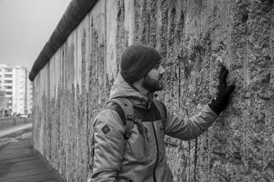 Young man wearing jacket touching weathered wall in city