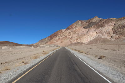 Road leading towards mountains against clear blue sky