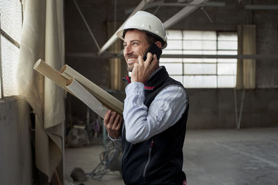 Smiling male building contractor talking over smart phone inside construction site